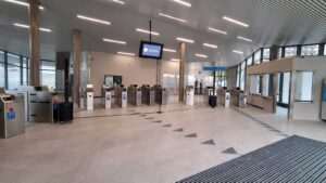 Vestíbulo de estación vacío, con torniquetes de control de acceso, columnas, fachada acristalada y una taquilla